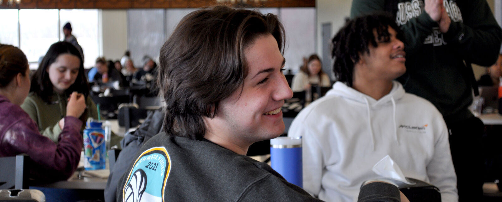 A male student looks off into the distance with a smile amidst other students in the Dining Hall