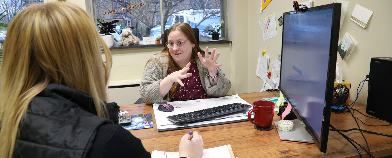 An employee in the Financial Aid office helps a student in her office