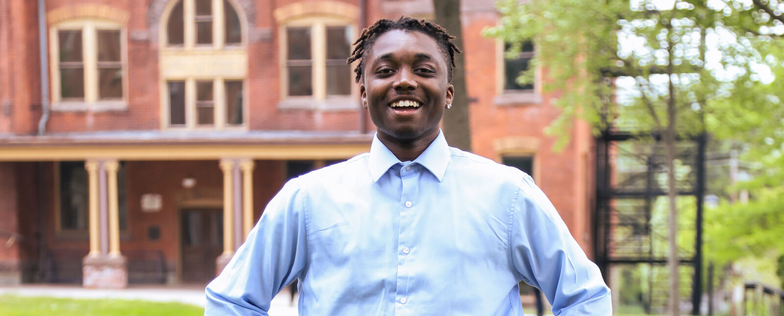 A male student poses in front of Cowles Hall wearing a light blue dress shirt