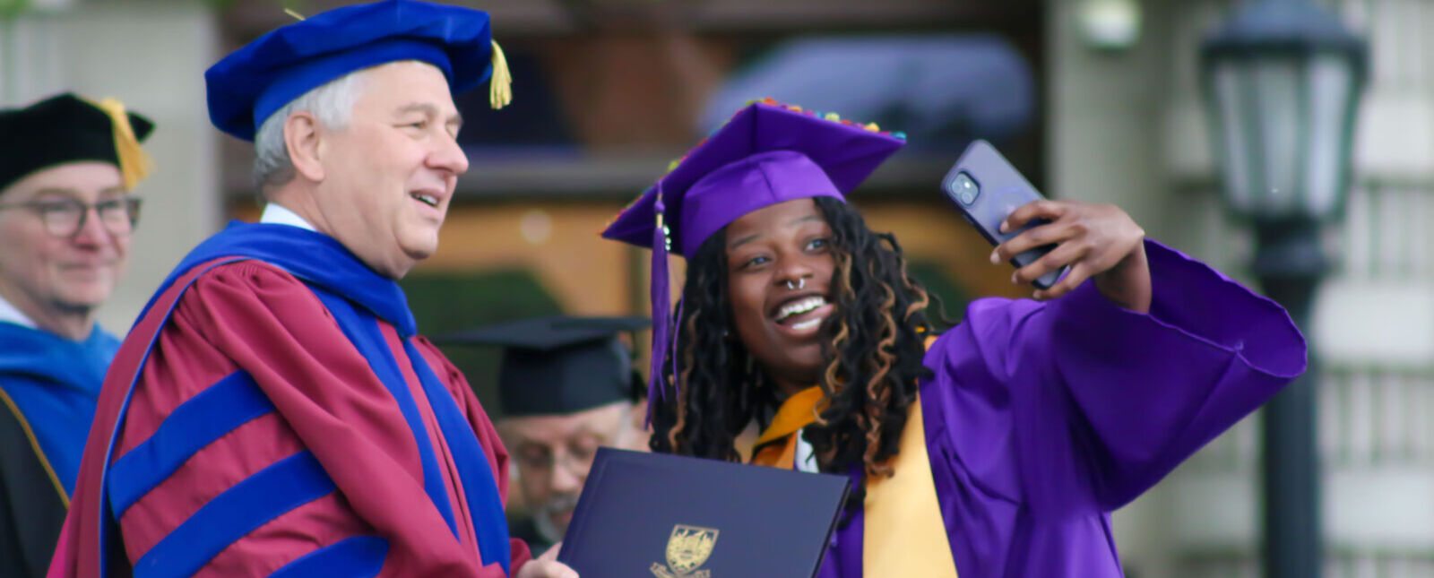 A female graduate takes an excited selfie with the Elmira College President.