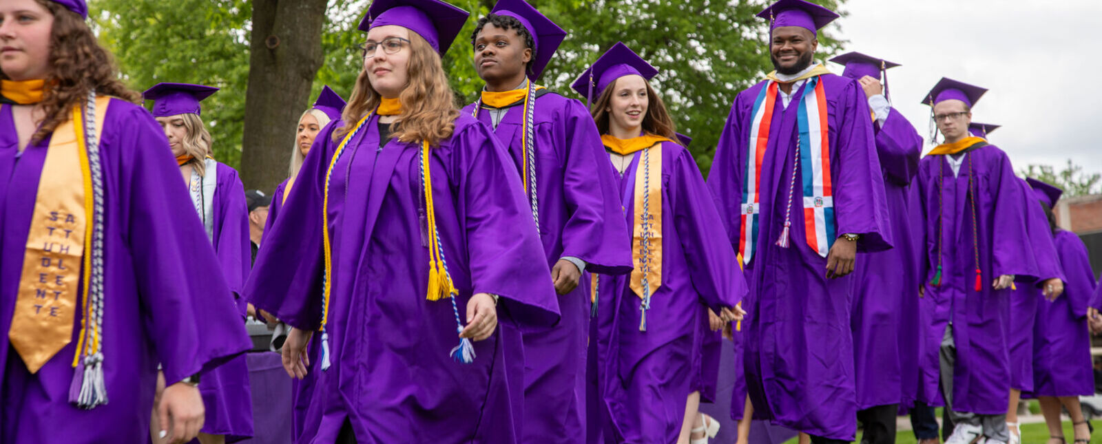 Some of the graduates smile as they proceed to their seats during Commencement