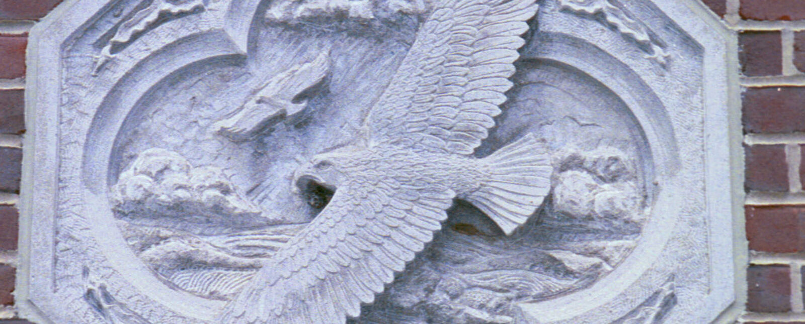 An octagon stone with an engraving of an eagle and scenery is mounted on a brick wall
