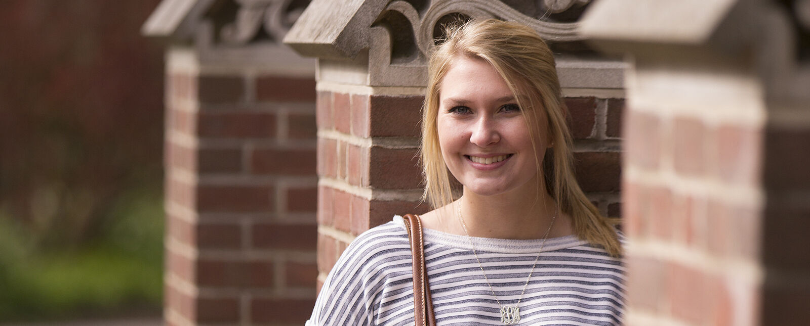 A female student poses against the brick entrance to an outdoor stairway