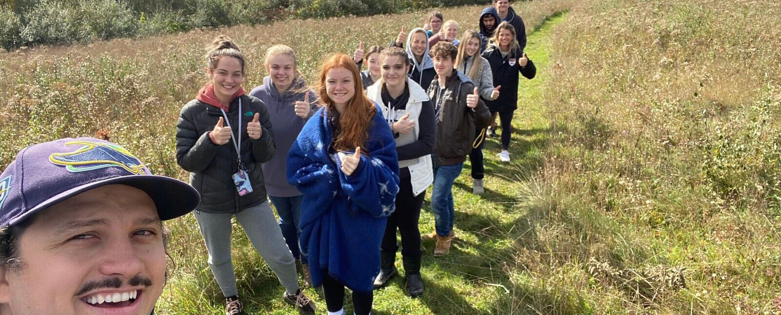 A group of students and a professor pose in a field during a Term III hiking trip