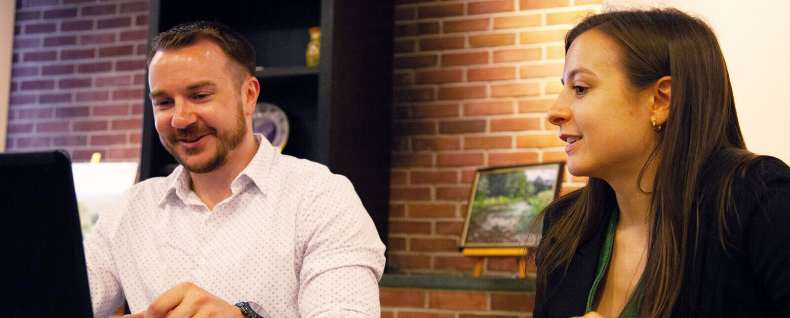 A male and female graduate student work on a laptop in a cafe