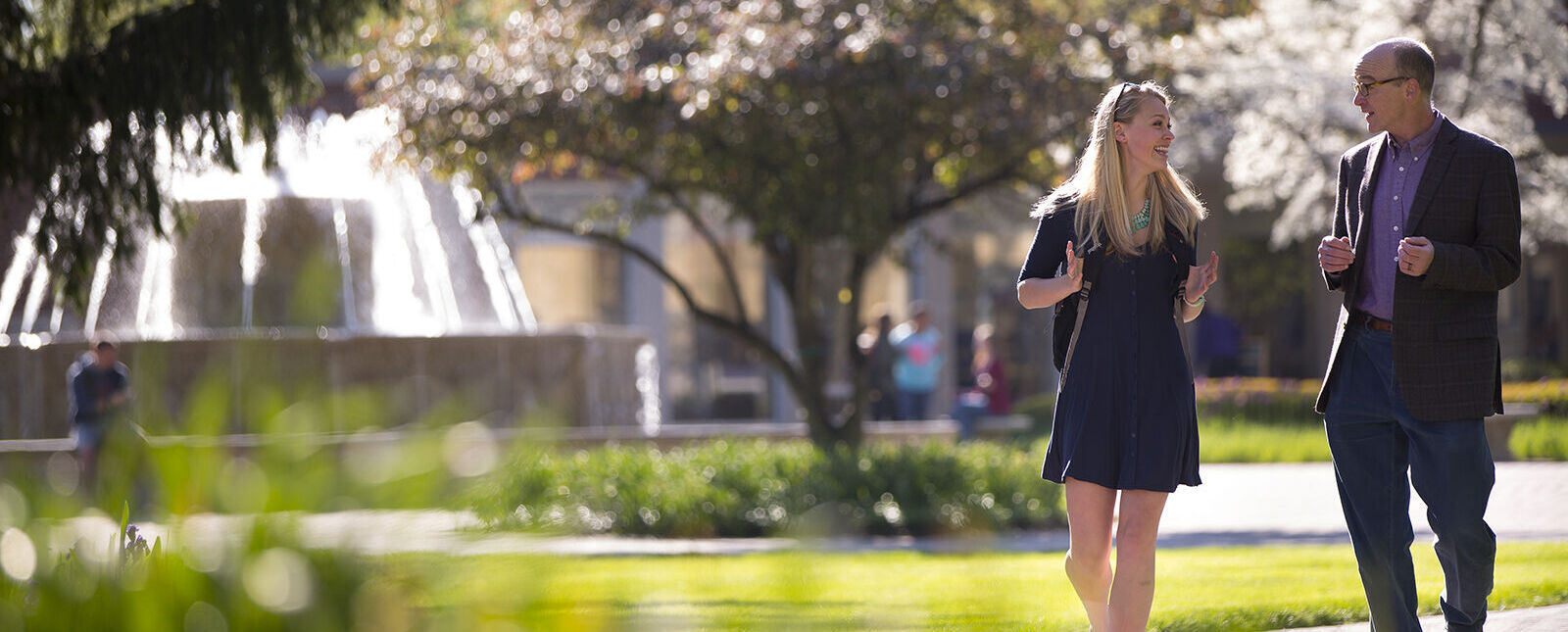 A teacher and student talk while walking across campus