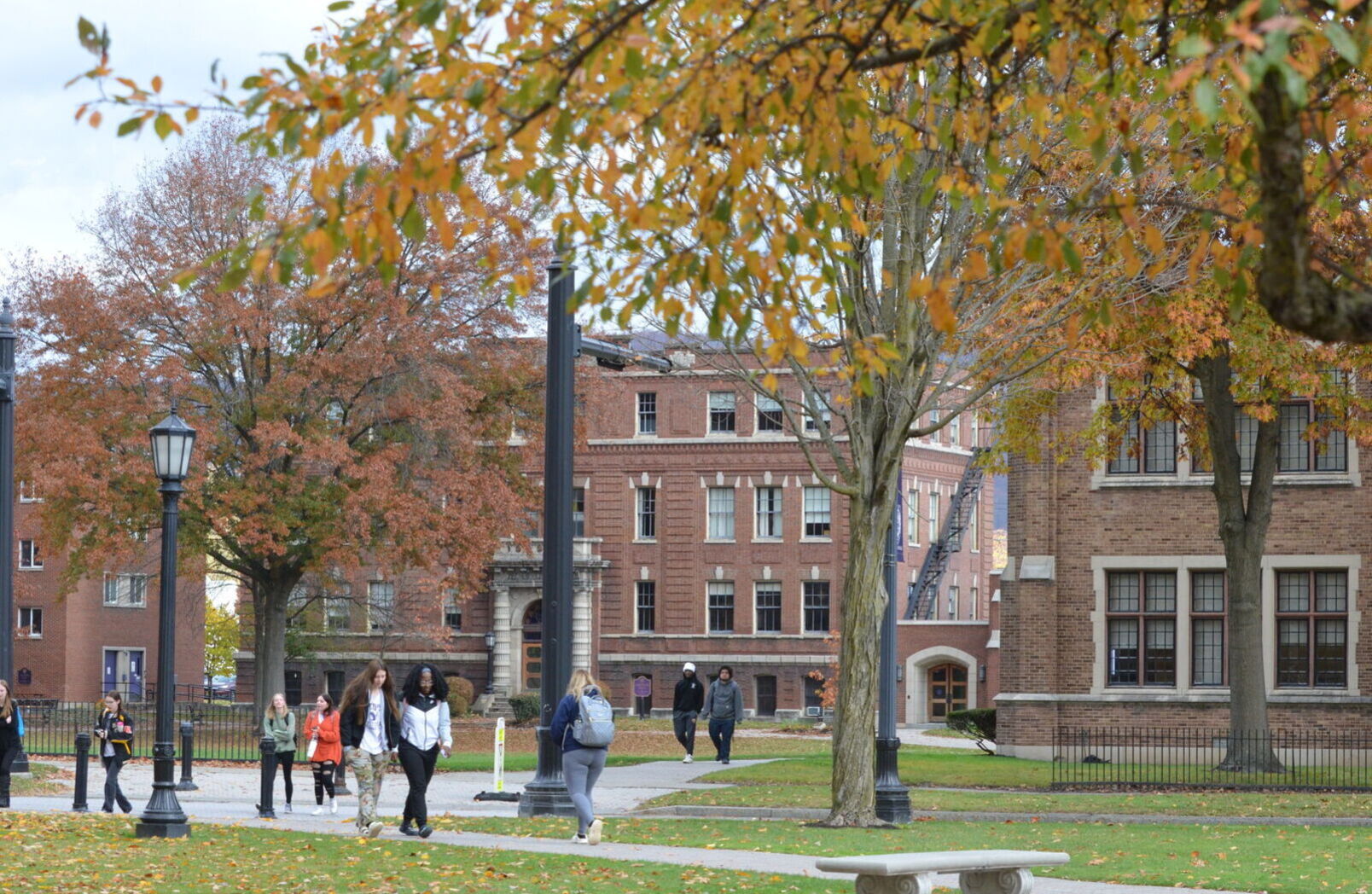 Students walk across campus surrounded by trees with colorful autumn leaves