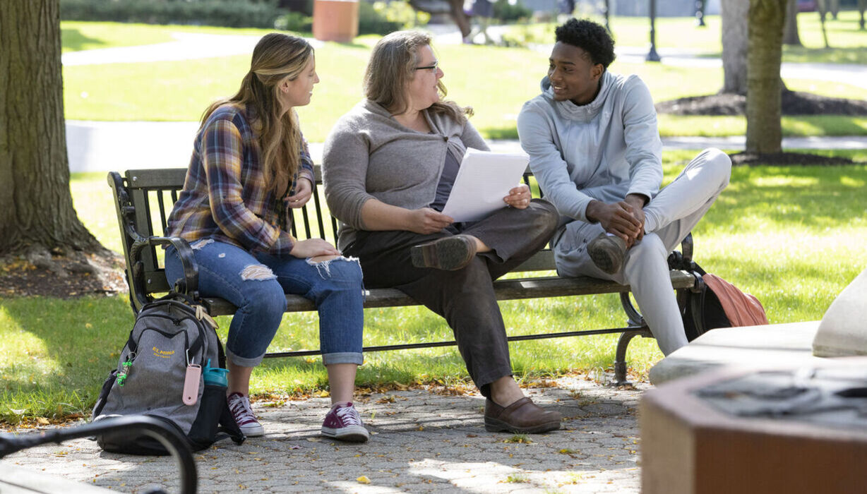Students and a professor chat on a bench