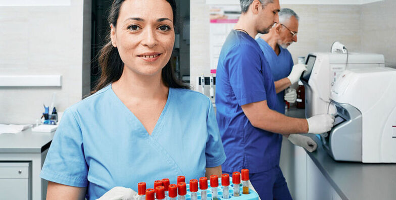 A female phlebotomy technician holds a tray of vials in a lab