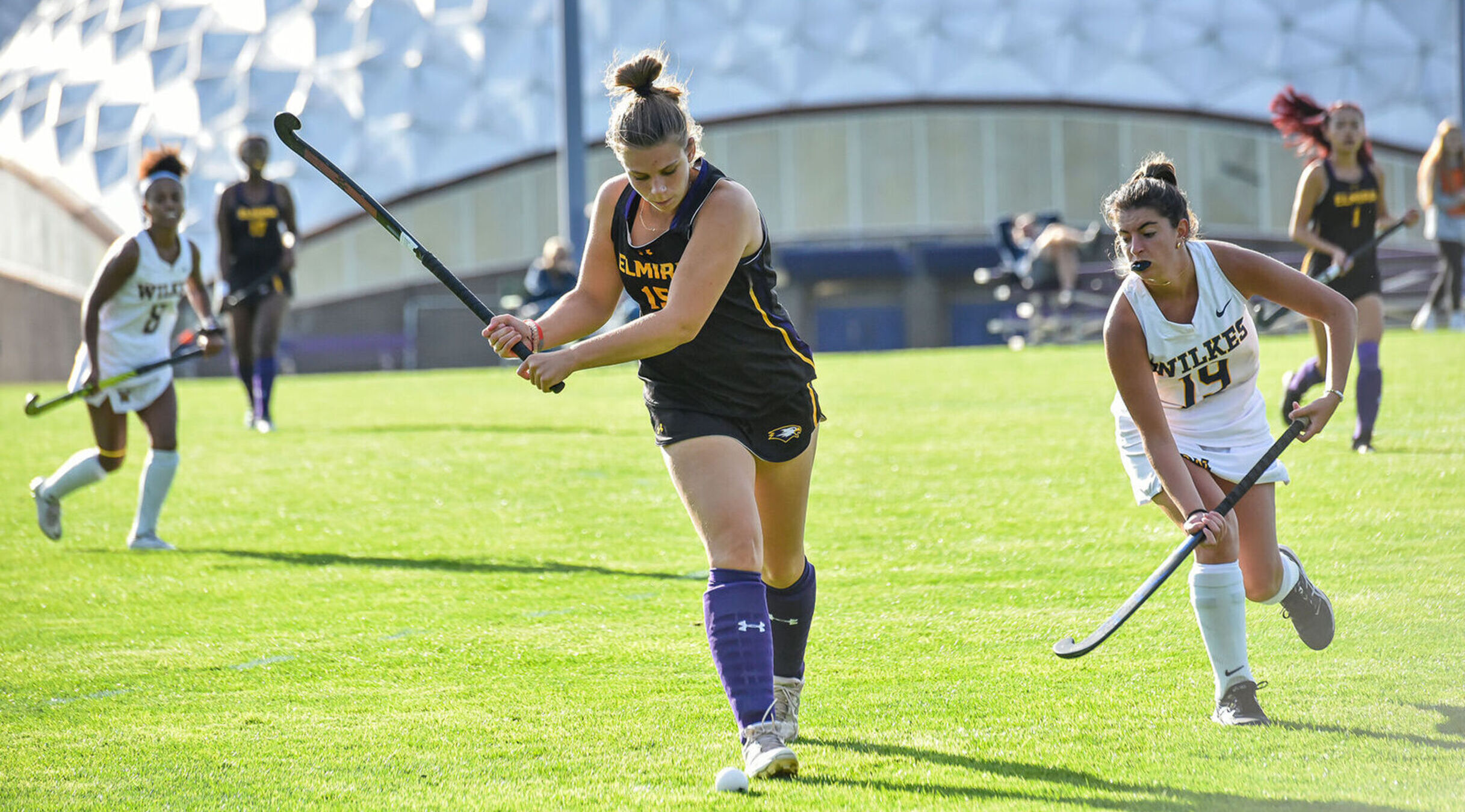 A field hockey player gets ready to hit the ball as a defender approaches