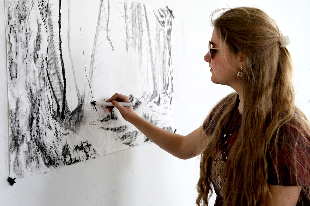A female Art Club member creates art on a wall during an Art Club meeting