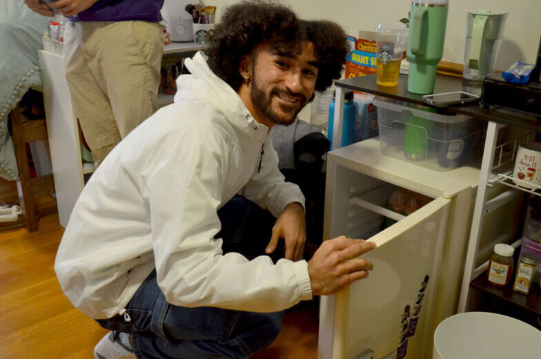 A male student smiles as he opens the mini refrigerator