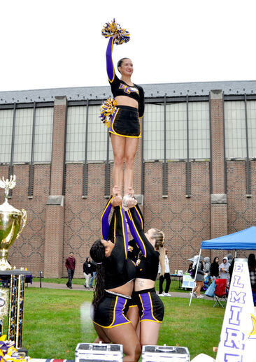 A cheerleader waves a pom pom in the air while being lifted high by her bases and backspot