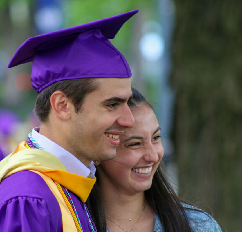 A male student in cap and gown stands with a female