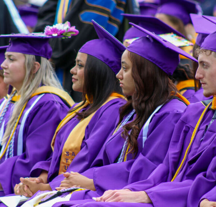 Students sit in their cap and gowns during Commencement