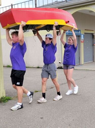 Three students carry a boat over their heads through Eldridge Park.