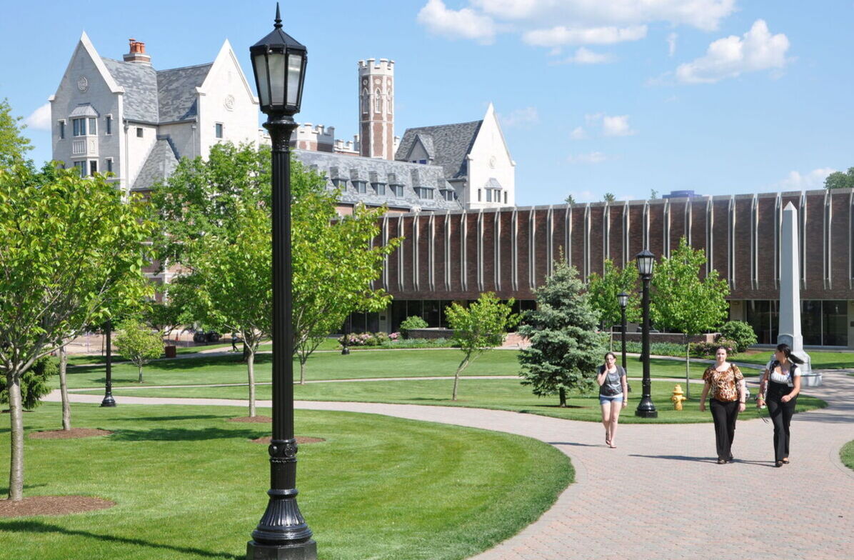 Students walk across campus with the Gannett-Tripp Library and Meier Hall in the background
