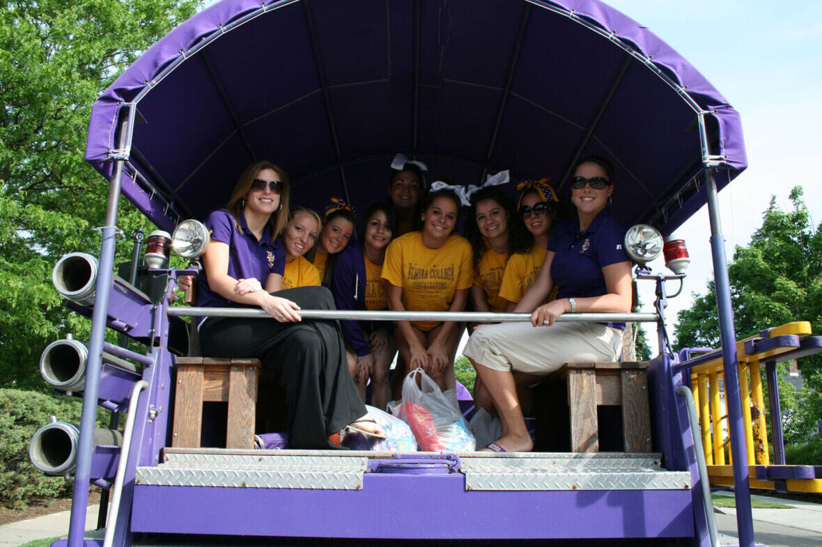 Cheerleaders an coaches sit in the back of a purple fire truck taking part in a parade