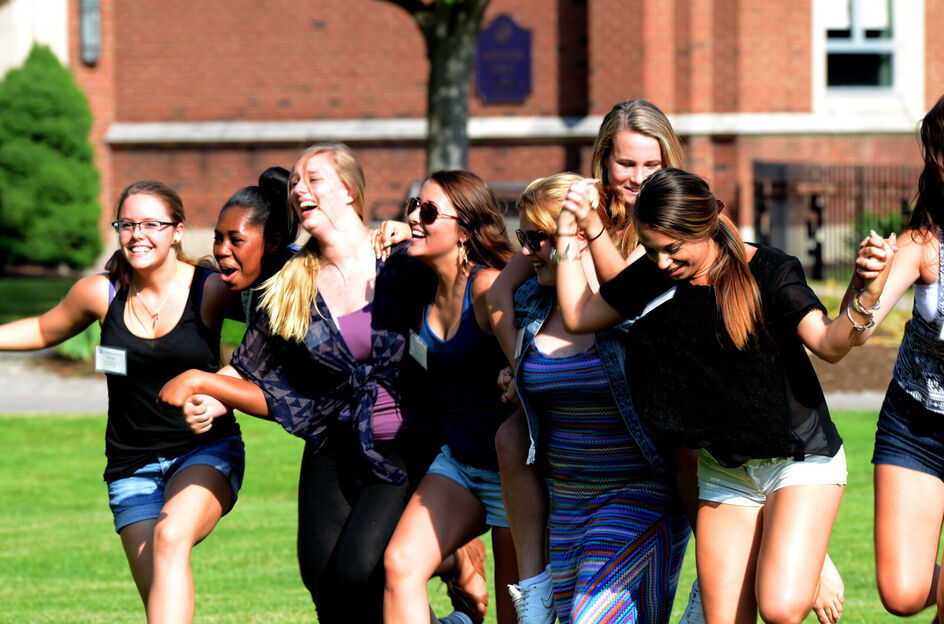 A group of female students hold hands while participating in an orientation activity on the campus lawn