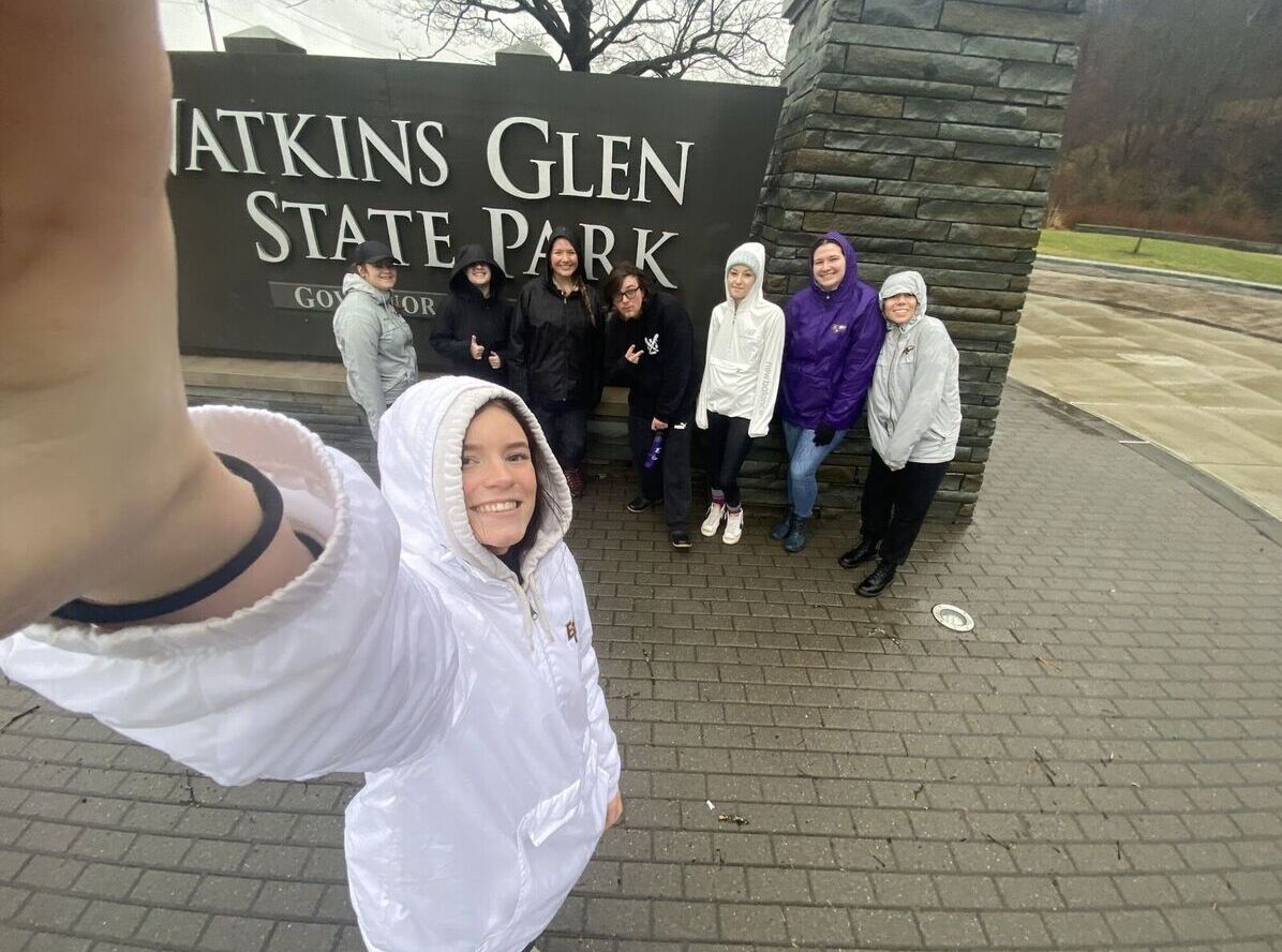 Hiking Club members pose for a group selfie in front of the Watkins Glen State Park sign