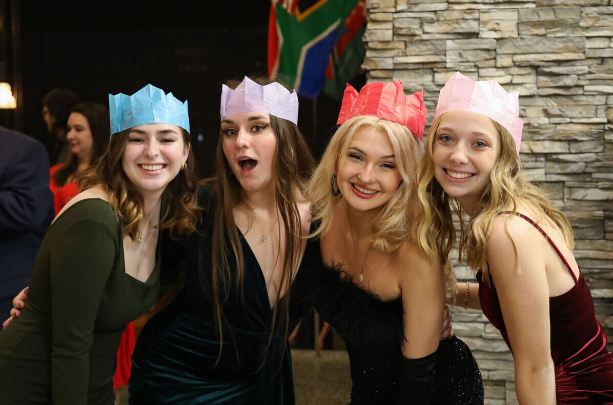 Four students pose for a picture while wearing paper crowns during the Holiday Banquet 