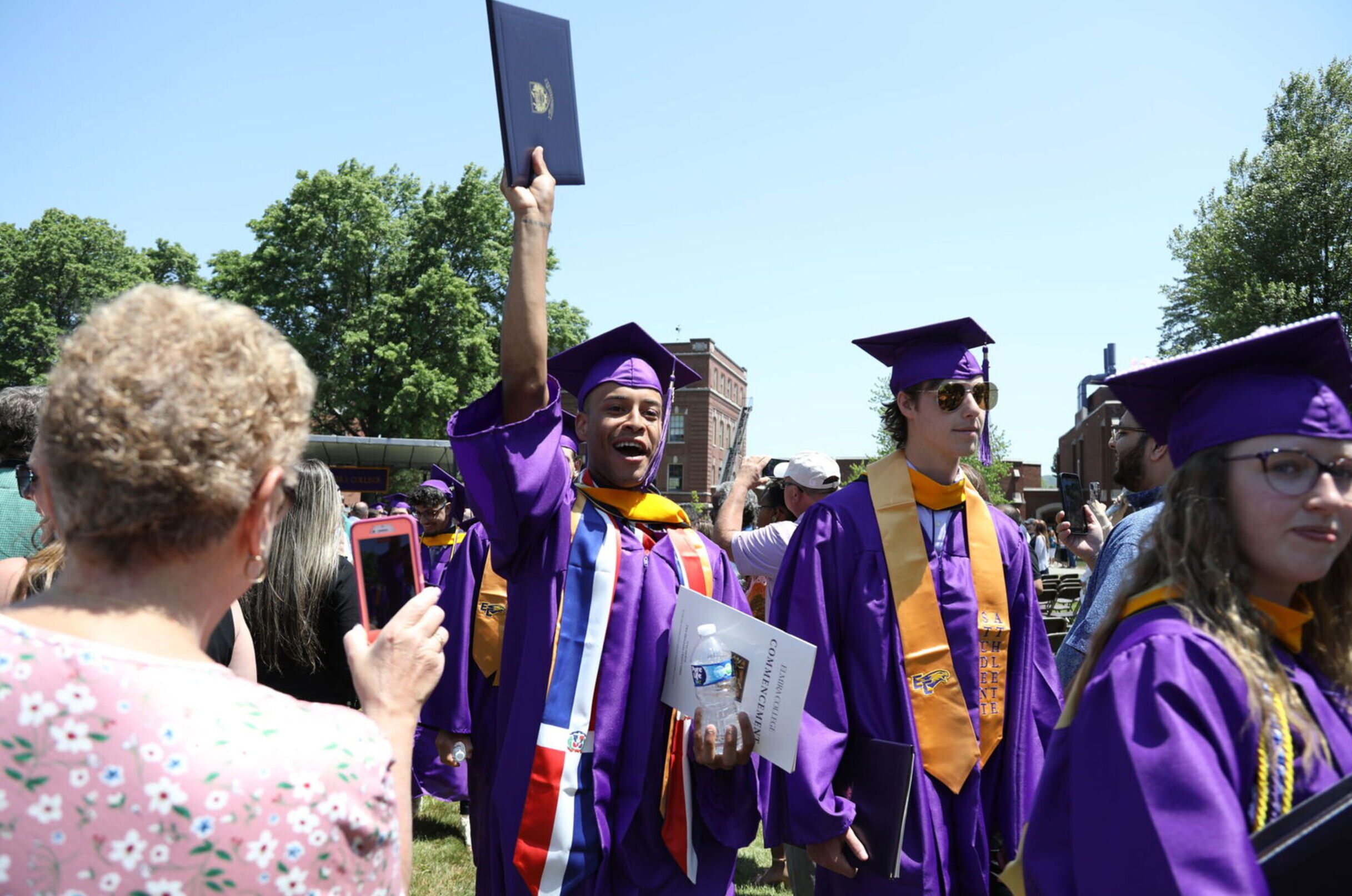 A male student raises his diploma high in the air as graduates proceed out of Commencement