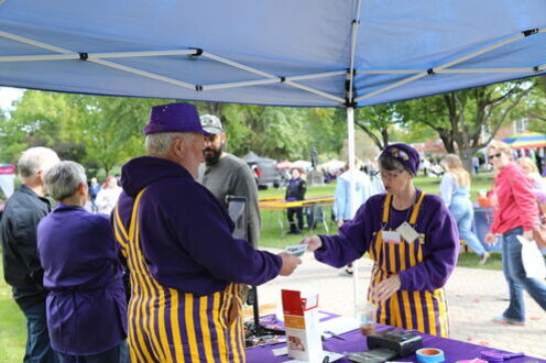 Octagon Fair participants work at a booth in purple and gold coveralls