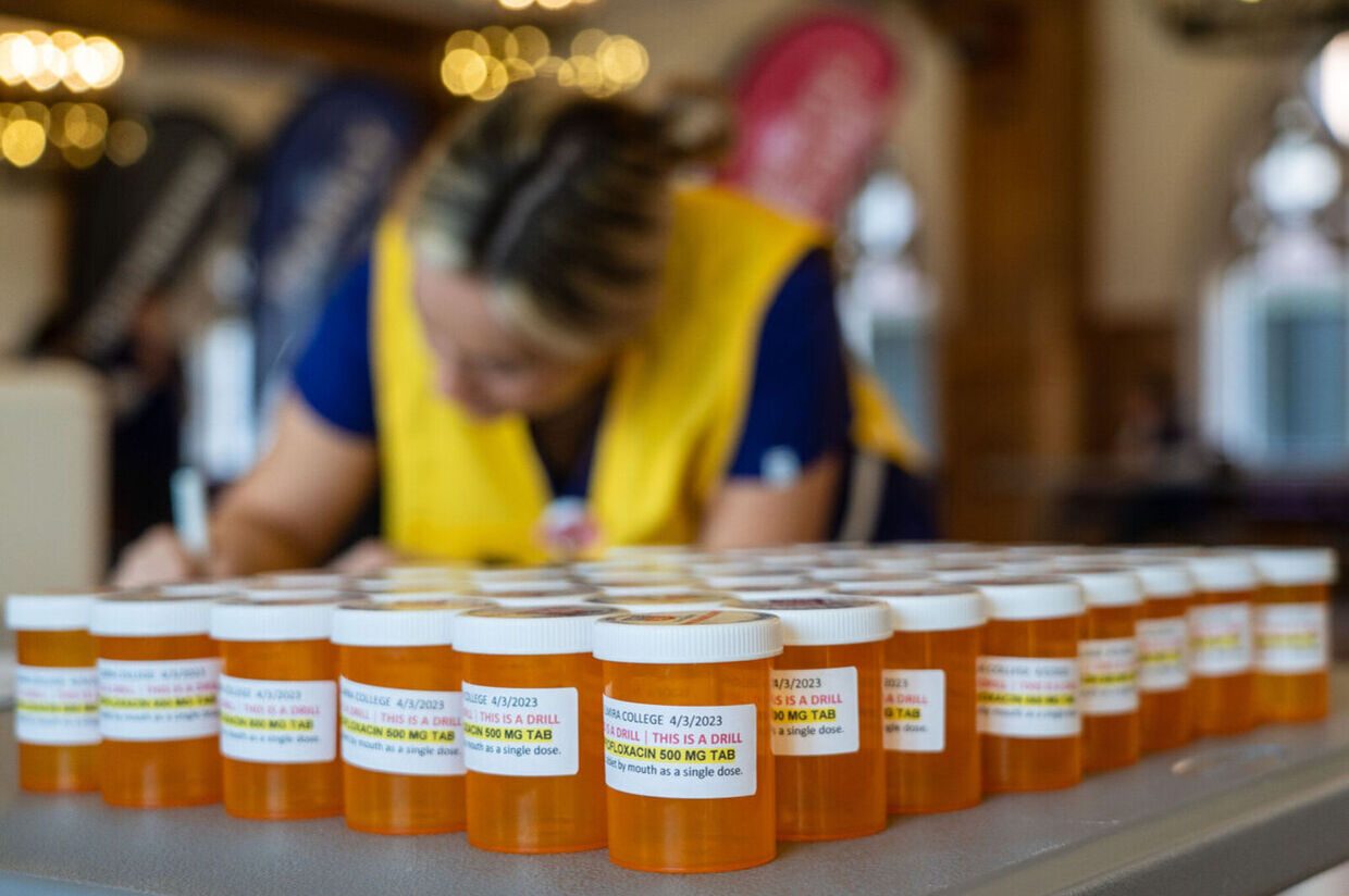 A nursing student fills out a form by a variety of medication bottles during an emergency drill 