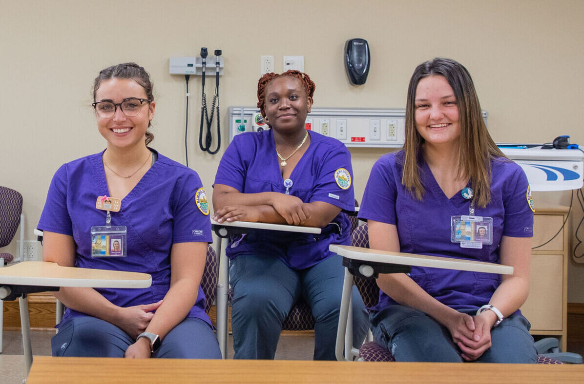 Three female nursing students smile while sitting at desks