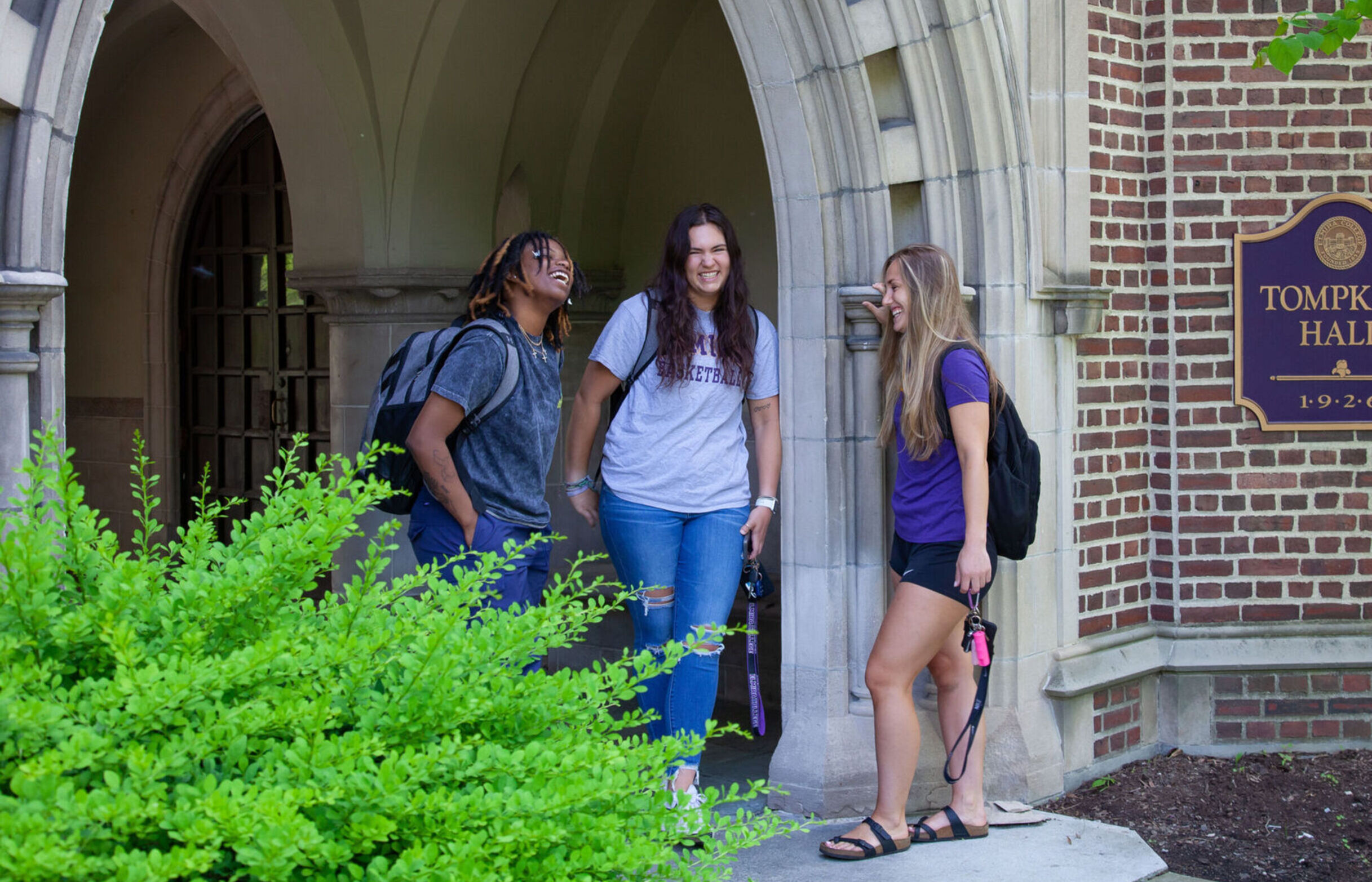 Three female students laugh while hanging out at the entrance of Tompkins Hall