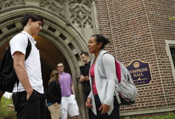 A male and female student talk and laugh near an entrance to Tompkins Hall as other students talk in the background