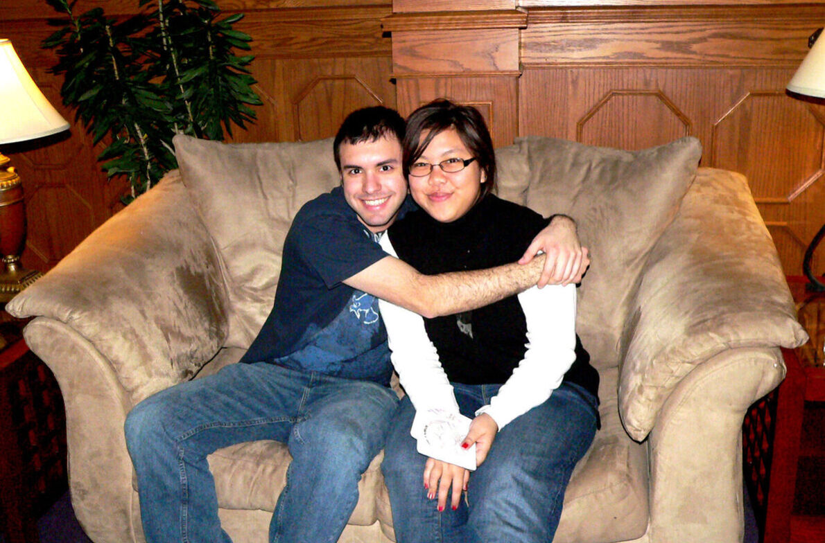 A male student hugs a female student while both sit in a plush chair