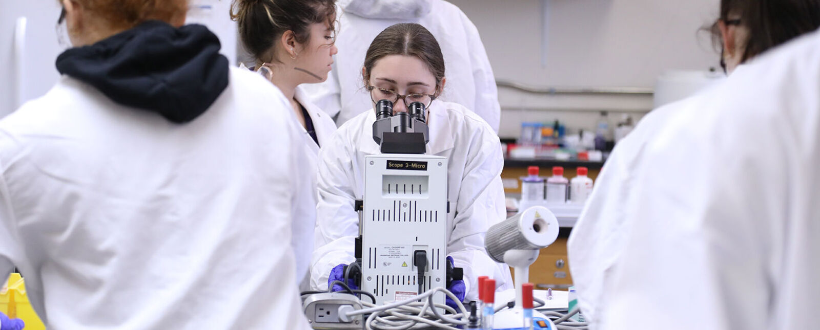 A female student looks through a microscope in a lab