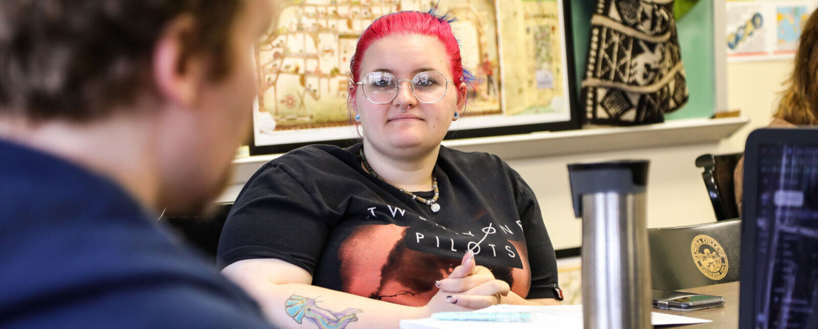 A student sits in a classroom speaking with a professor. 