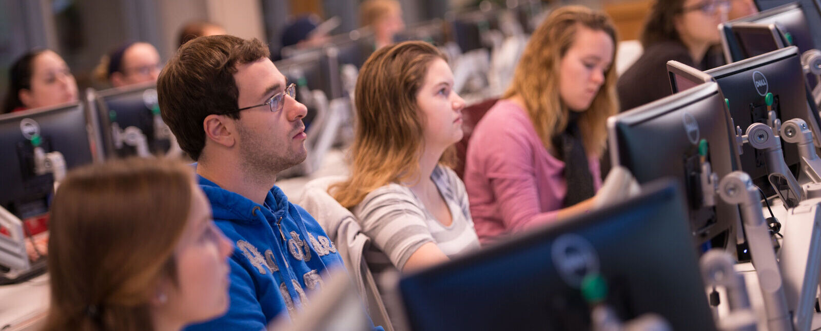 Students listen while sitting at the computers in the Malesardi Finance Trading Room